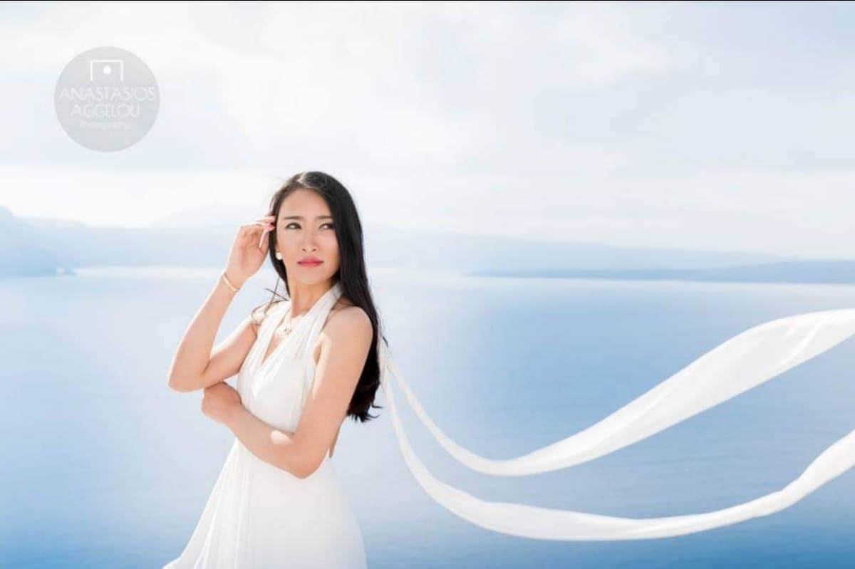Asian bridal look with flowing veil over Santorini caldera
